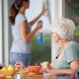 Senior woman having breakfast with home care in the background